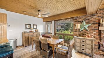 A dining area with a wooden table and chairs, a brick wall with a star decoration, and a view of greenery outside.