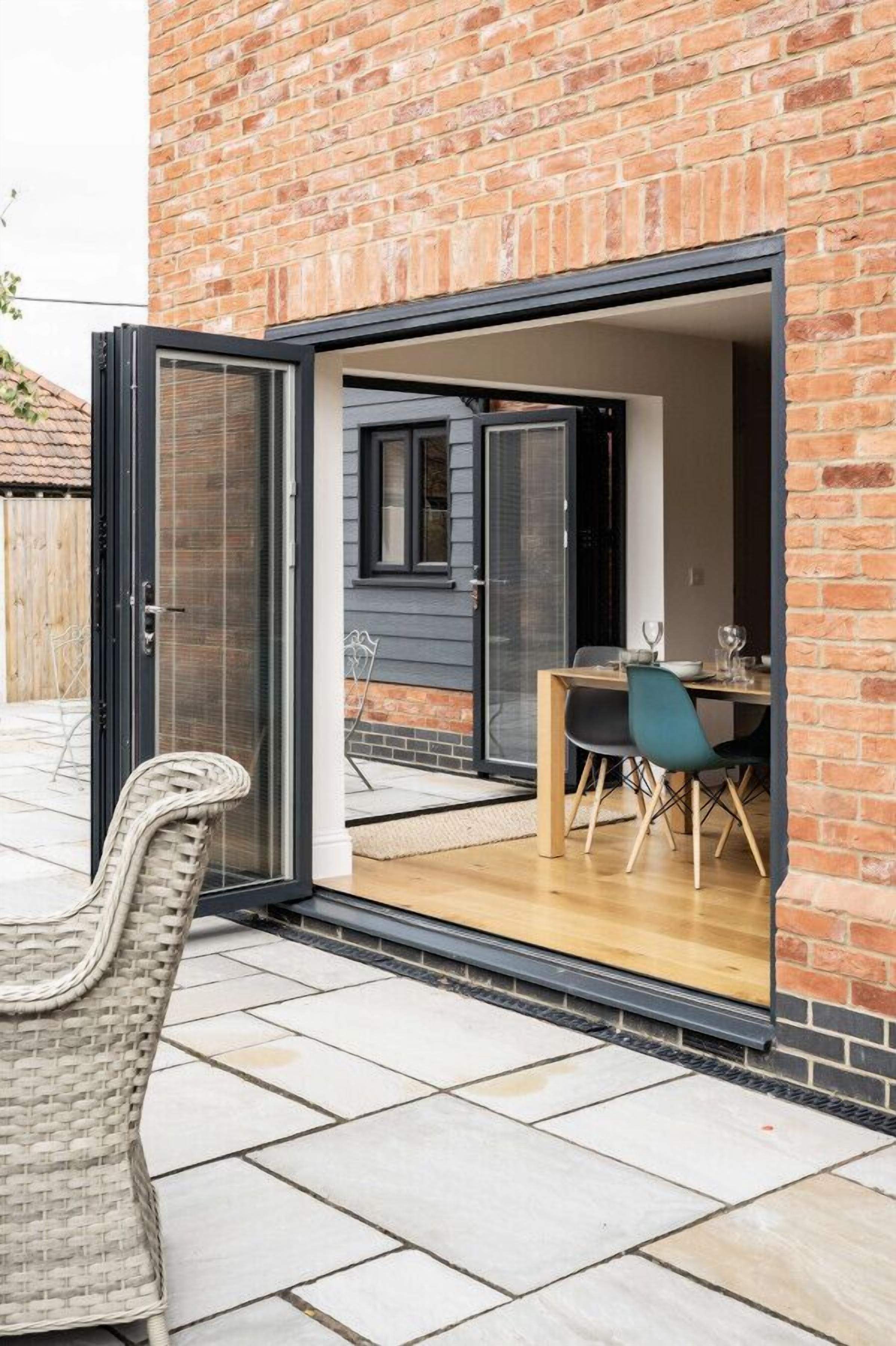 A modern house with a brick exterior, a sliding glass door leading to a dining area with a table and chairs, and a wicker chair outside.