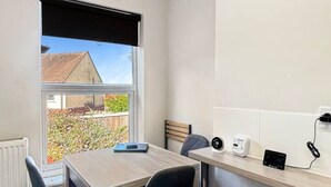 Una cocina moderna con una mesa de madera, dos sillas, una ventana con vistas a una casa y un radio montado en la pared.
