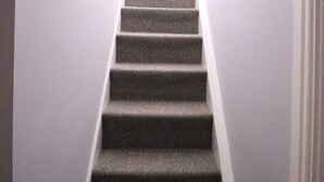 Una escalera alfombrada en un pasillo con paredes blancas y una puerta a la derecha.