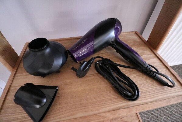 A hair dryer, a charging cable, and a power adapter on a wooden surface.
