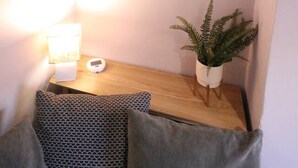 Una habitación acogedora con un escritorio de madera, una pequeña planta en maceta, un espejo y un cojín estampado.
