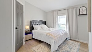 Une chambre à coucher avec un lit, une table de chevet, une lampe et une fenêtre avec des rideaux.