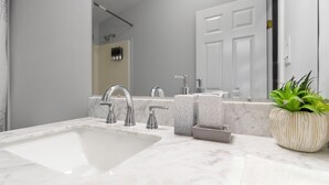 Une salle de bain moderne avec un grand lavabo, deux robinets, un miroir et une plante en pot.