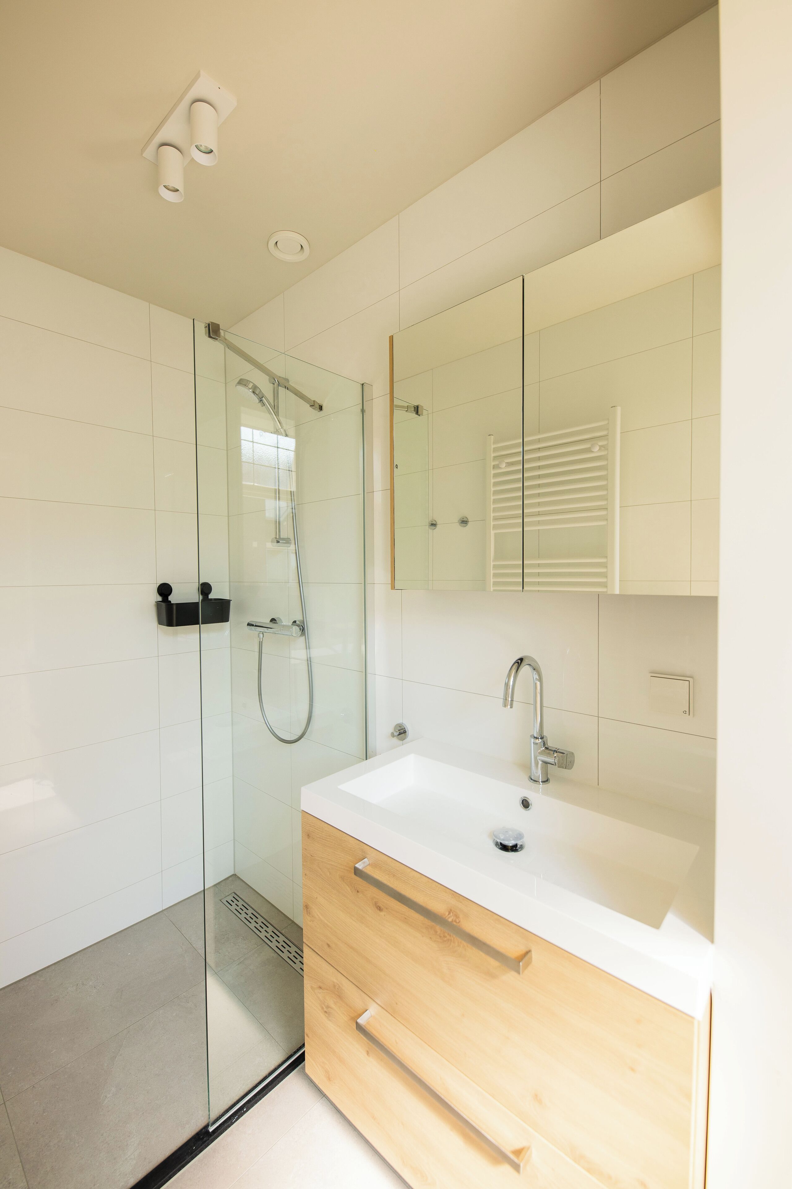 A modern bathroom with a glass-enclosed shower, a white sink, and a wooden vanity.