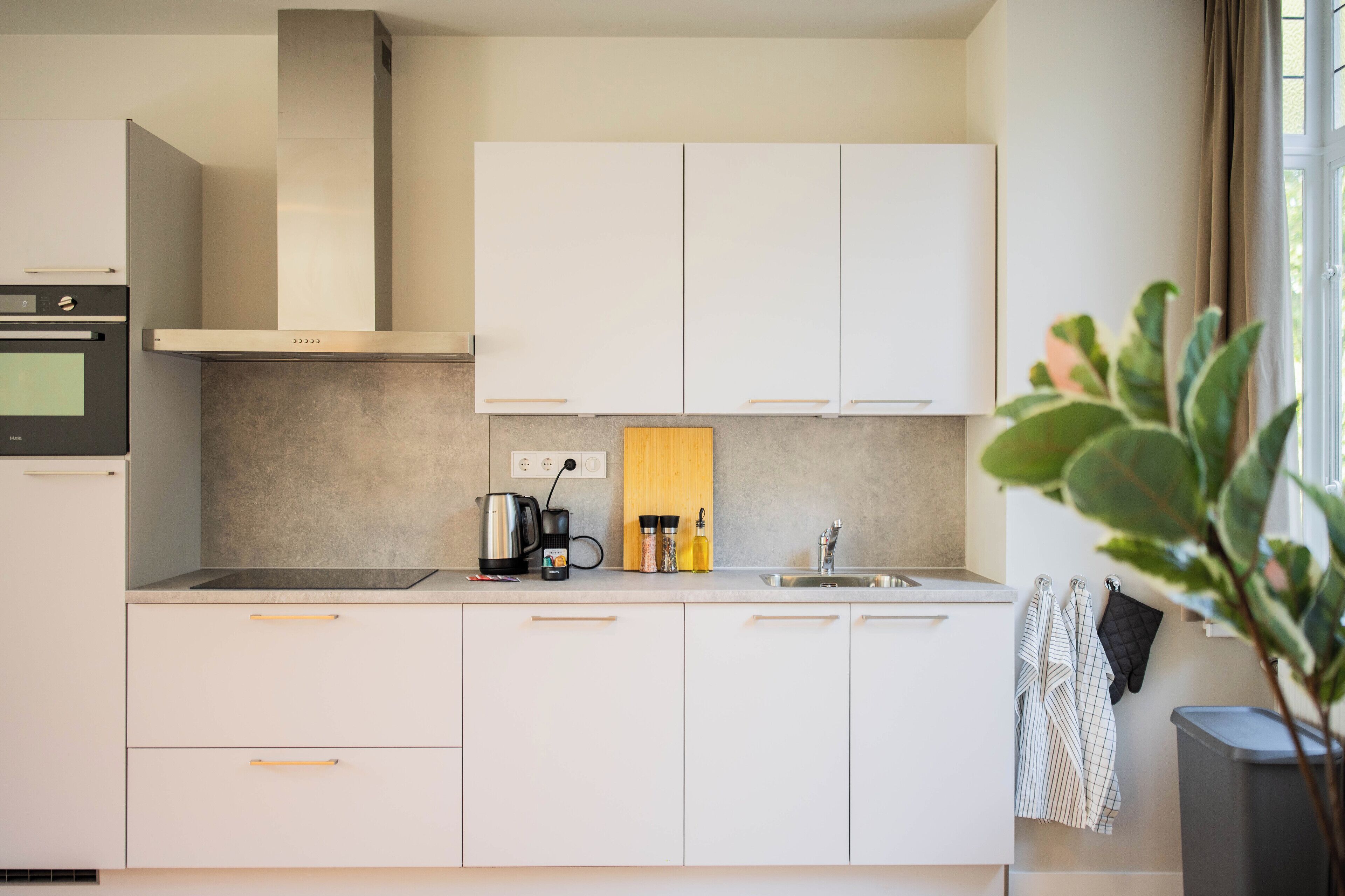 Una cocina moderna con armarios blancos, una campana extractora de acero inoxidable, una cafetera y un fregadero.