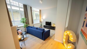 A modern living room with a blue sofa, a TV, and a large illuminated letter 'I' on the wall. - Alphabet Apartments Westersingel (Rotterdam)
