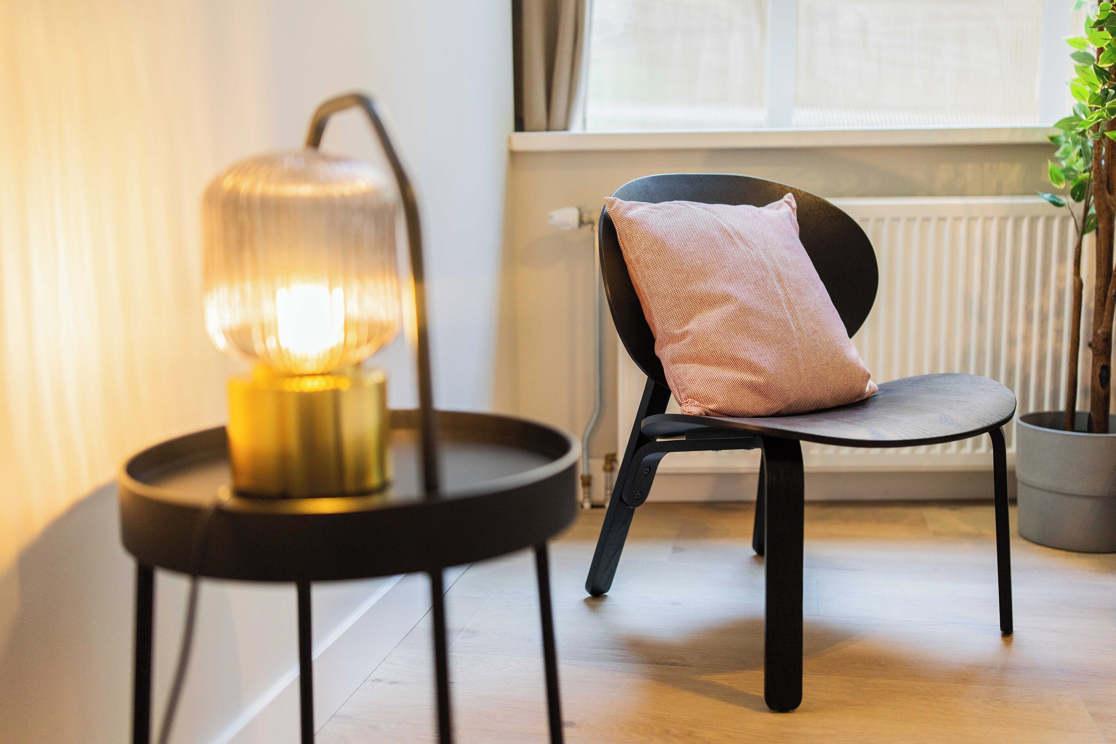 A modern room with a round black table, a chair with a cushion, and a floor lamp.