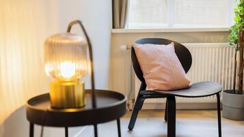 A modern room with a round black table, a chair with a cushion, and a floor lamp.