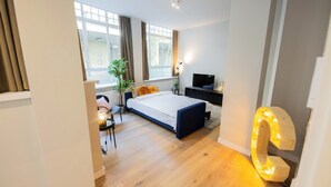 A modern bedroom with a bed, a desk, a TV, and a large illuminated '2' sign. - Alphabet Apartments Westersingel (Rotterdam)