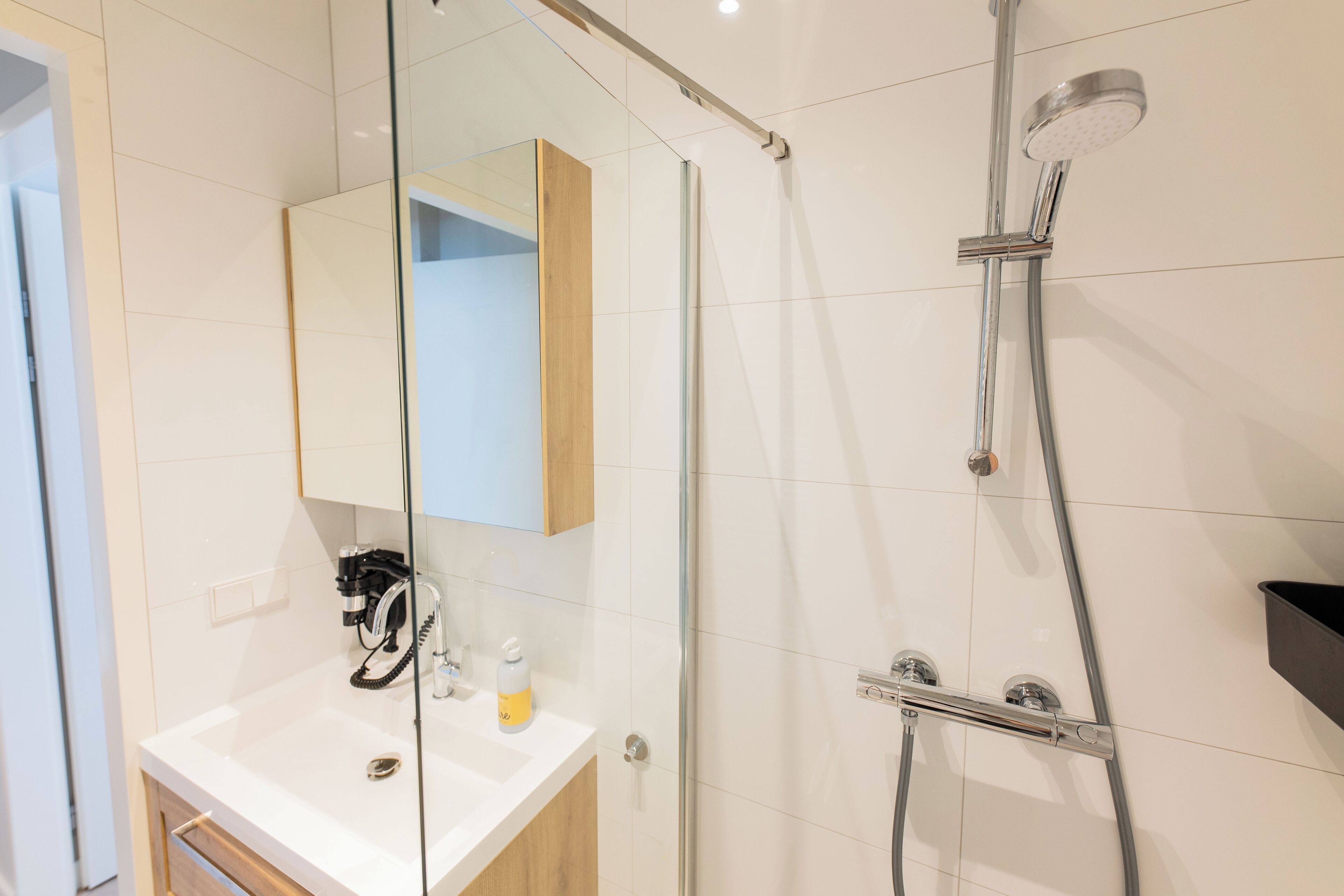 A modern bathroom with a glass shower enclosure, a white sink with a mirror, and a wooden cabinet.