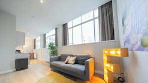 A modern living room with a grey sofa, a round rug, and a wall-mounted light fixture. - Alphabet Apartments Westersingel (Rotterdam)