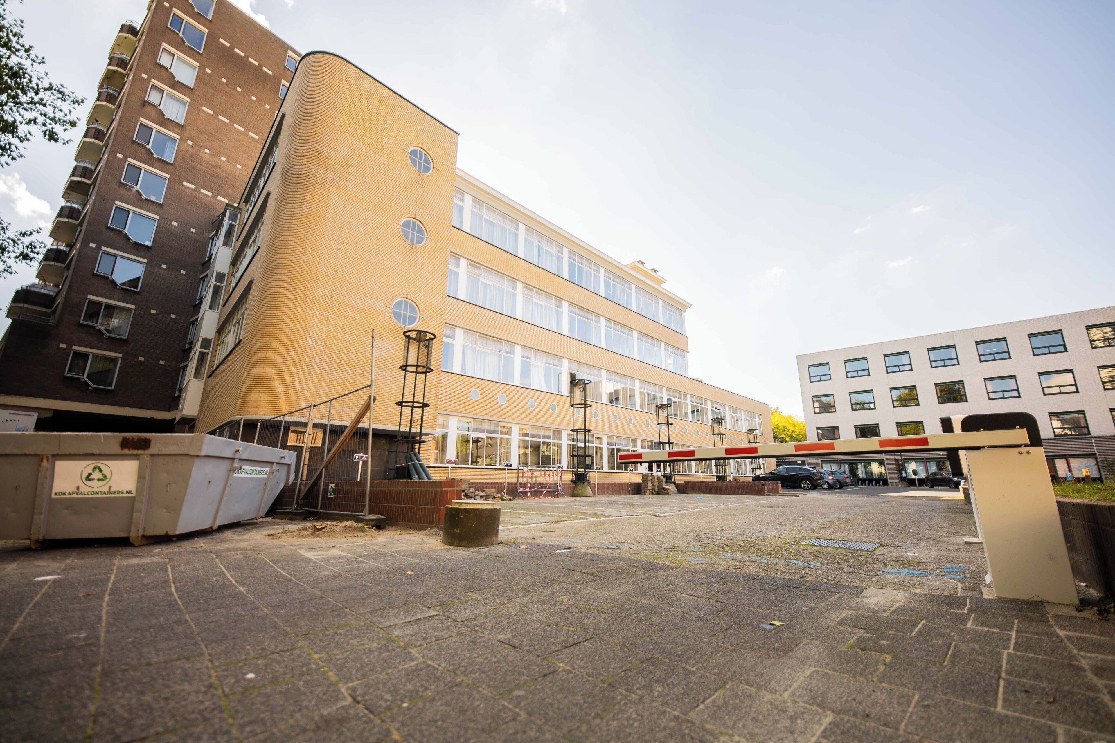Een meerlaags gebouw met een gebogen gevel, een parkeerplaats met overdekte ingang, en een afvalbak met de tekst 