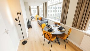 A modern dining area with a round table, yellow chairs, and a sofa in the background. - Alphabet Apartments Westersingel (Rotterdam)
