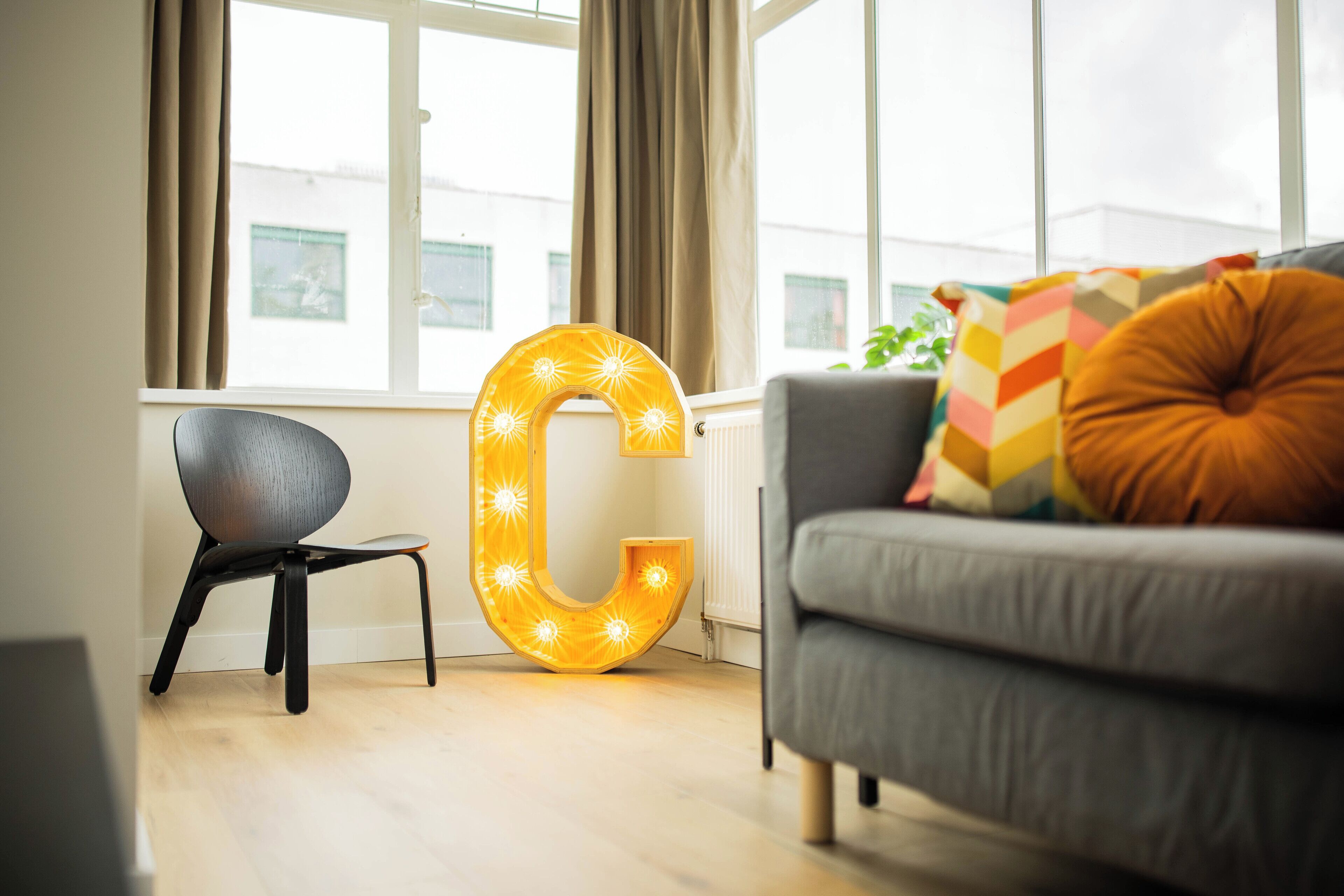 A modern living room with a large illuminated 'C' sign, a grey sofa, and a small black chair.