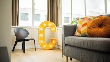 A modern living room with a large illuminated 'C' sign, a grey sofa, and a small black chair.