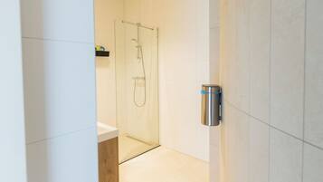 Une salle de bain moderne avec une douche à parois de verre, un lavabo blanc et un distributeur de serviettes en acier inoxydable.