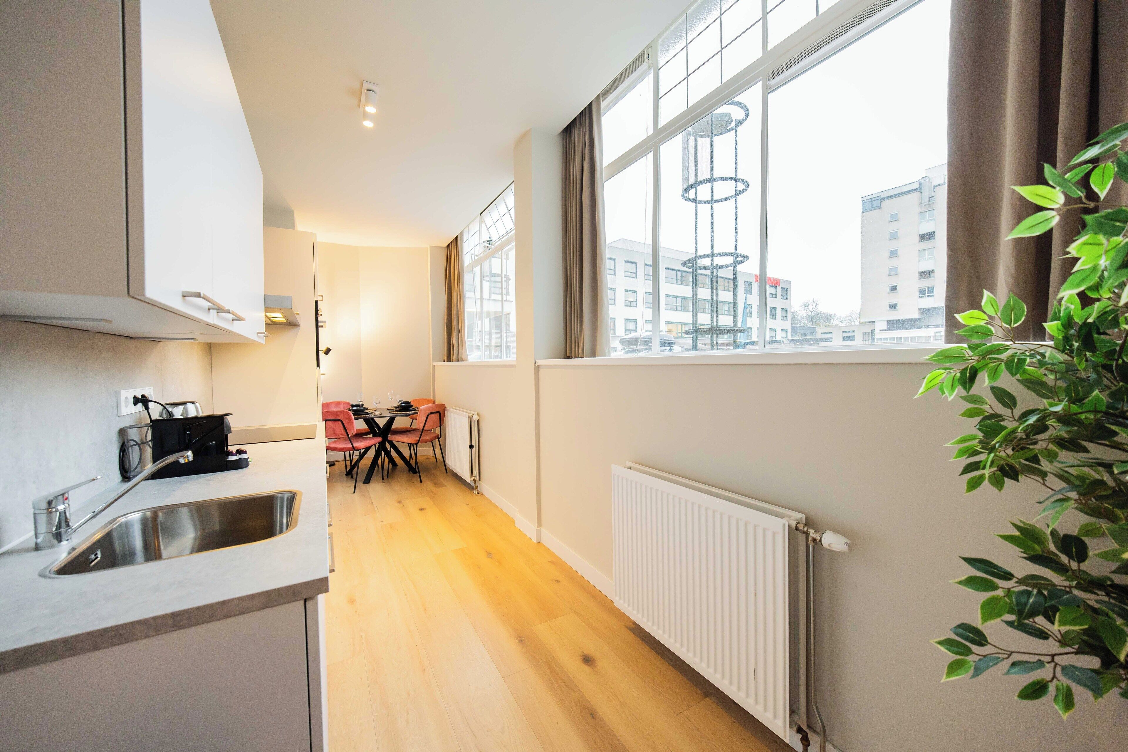 A modern kitchen with a built-in sink, a dining area with a table and chairs, and a large window with a city view.