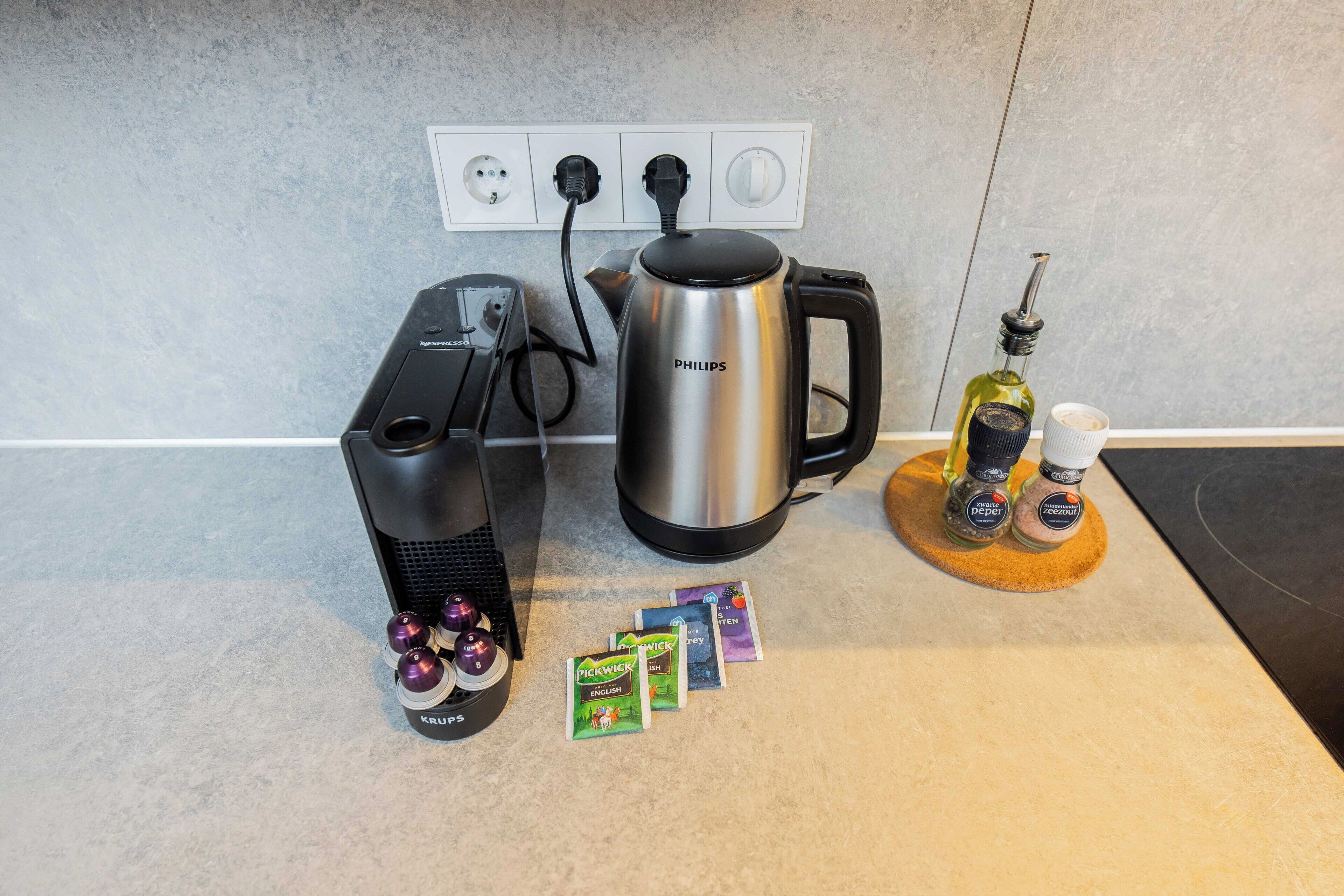 Una cocina con cafetera, hervidor y algunos pods de café sobre la encimera.