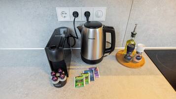 Una cocina con cafetera, hervidor y algunos pods de café sobre la encimera.