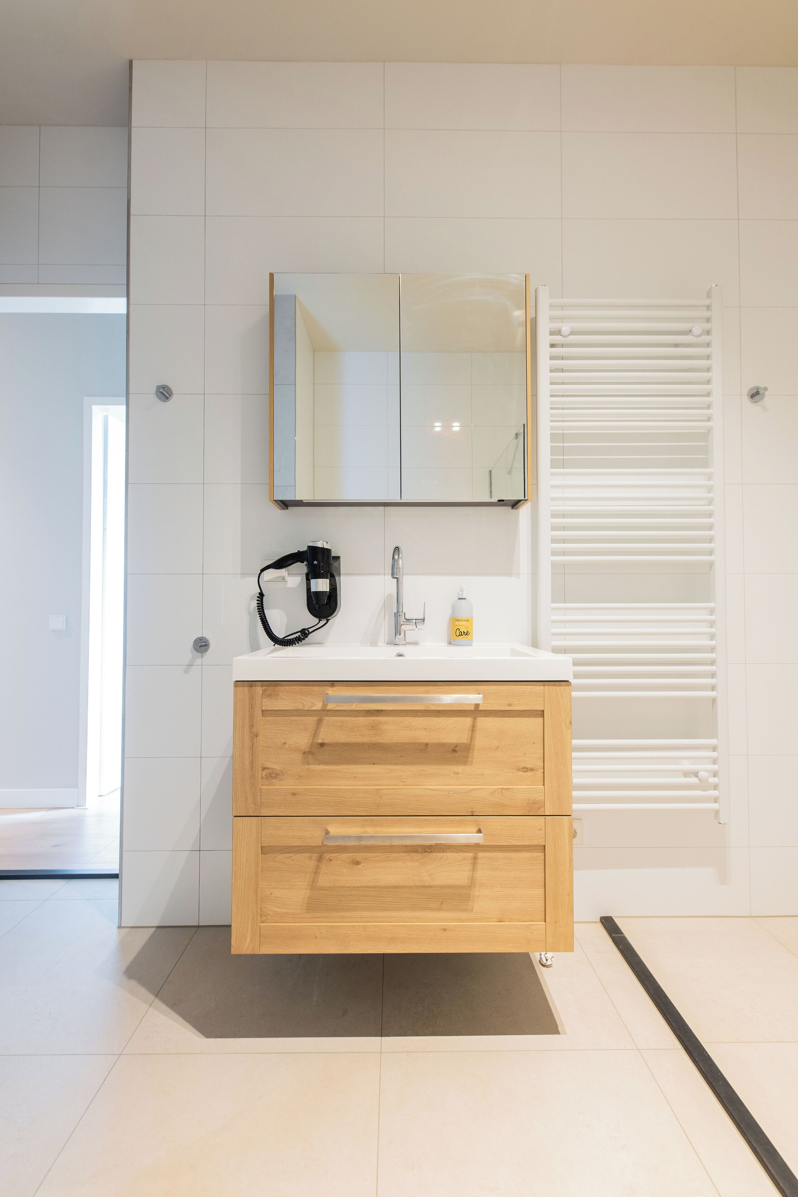Een moderne badkamer met een witte wastafel, een spiegel, een handdoekrek en een douche.