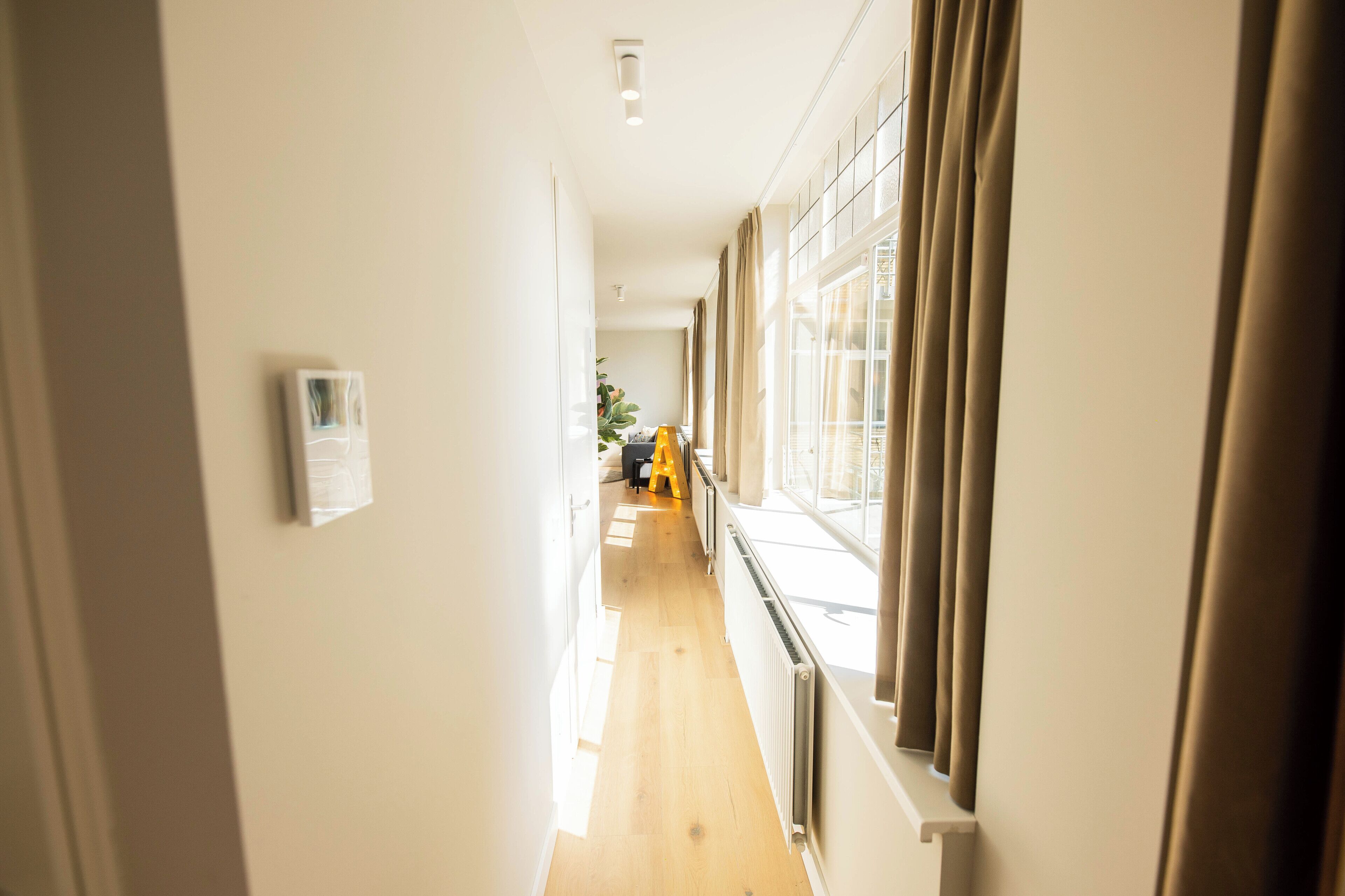A hallway with a radiator, a thermostat, and a yellow chair.
