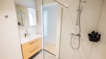 Een moderne badkamer met een douchecabine van glas, een witte wastafel met spiegel en een houten opbergmeubel.