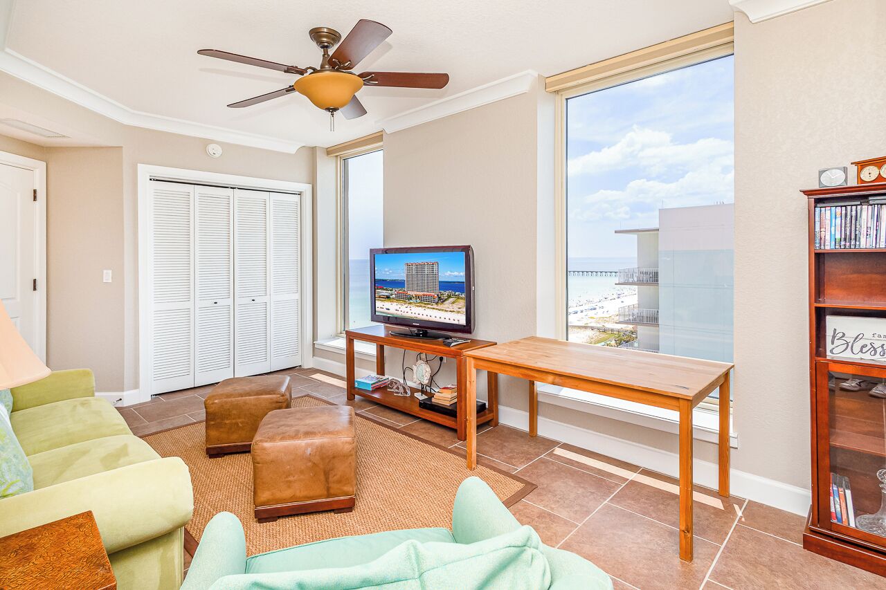 Un salon avec une télévision, une bibliothèque, un ventilateur de plafond et une vue sur la plage.