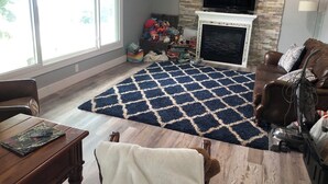 A living room with a fireplace, a television mounted above it, and a large window providing natural light. - Family-Friendly Lakeside Getaway in the Heart of Traverse City! (Traverse City)