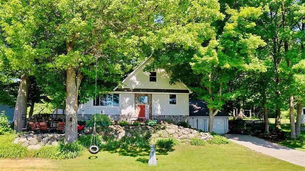 A single-story house with a red door, surrounded by trees and a well-maintained lawn. - Family-Friendly Lakeside Getaway in the Heart of Traverse City! (Traverse City)