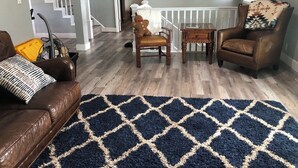A living room with a dark blue and beige rug, a brown leather sofa, a wooden coffee table, a brown leather armchair, and a teddy bear on a chair. - Family-Friendly Lakeside Getaway in the Heart of Traverse City! (Traverse City)