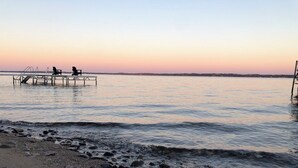 A beach with a wooden pier extending into calm waters, a rocky shoreline, and a sunset in the background. - Family-Friendly Lakeside Getaway in the Heart of Traverse City! (Traverse City)
