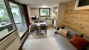 A compact kitchen with a dining area, a sofa, and a window with a view of houses.