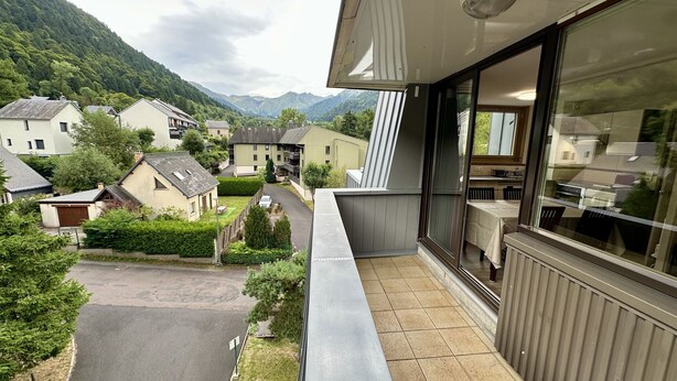 A balcony with a view of a residential area, a road, and mountains in the background.