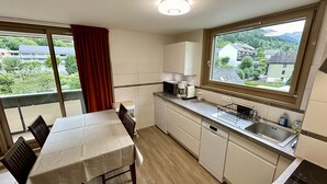 A compact kitchen with a dining area, a large window with a view of buildings and greenery, and basic amenities.