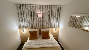 A bedroom with a bed, two bedside tables, a wall-mounted lamp, and a mirror.