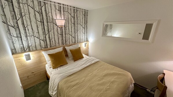 Une chambre à coucher comprenant un lit, une table de chevet, une lampe fixée au mur et un miroir.