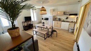 A compact kitchen with wooden cabinets, a dining table with benches, a TV on a stand, and a potted plant.