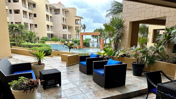 Une terrasse sur le toit, aménagée avec du mobilier d’extérieur, des plantes en pot et offrant une vue sur une piscine et des bâtiments.