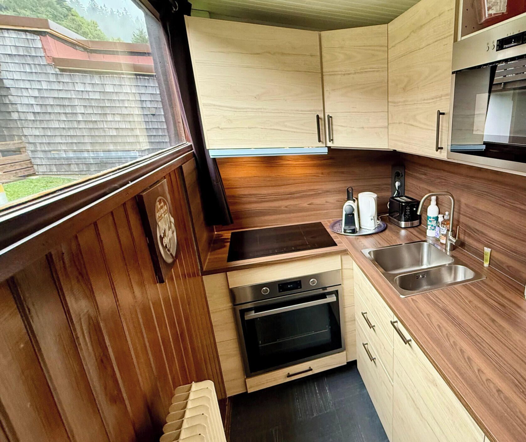 A compact kitchen with wooden cabinets, a built-in oven, a sink, and a coffee maker.
