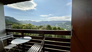 A balcony with a table and chairs, overlooking a mountainous landscape.
