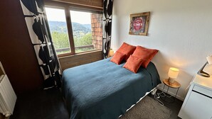 A bedroom with a bed, a nightstand, a lamp, and a window with a view of the countryside.
