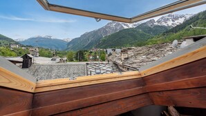 A view from a wooden balcony with a skylight, overlooking a mountainous landscape with snow-capped peaks and a valley below.
