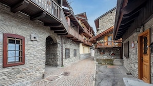 A narrow cobblestone alley with stone buildings, wooden balconies, and a small water feature.