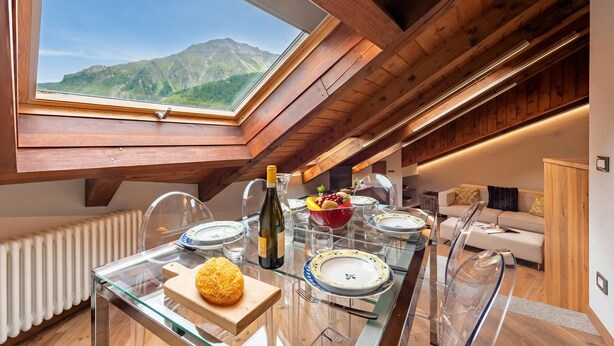A dining area with a table set for four, a bottle of wine, and a bowl of fruit.