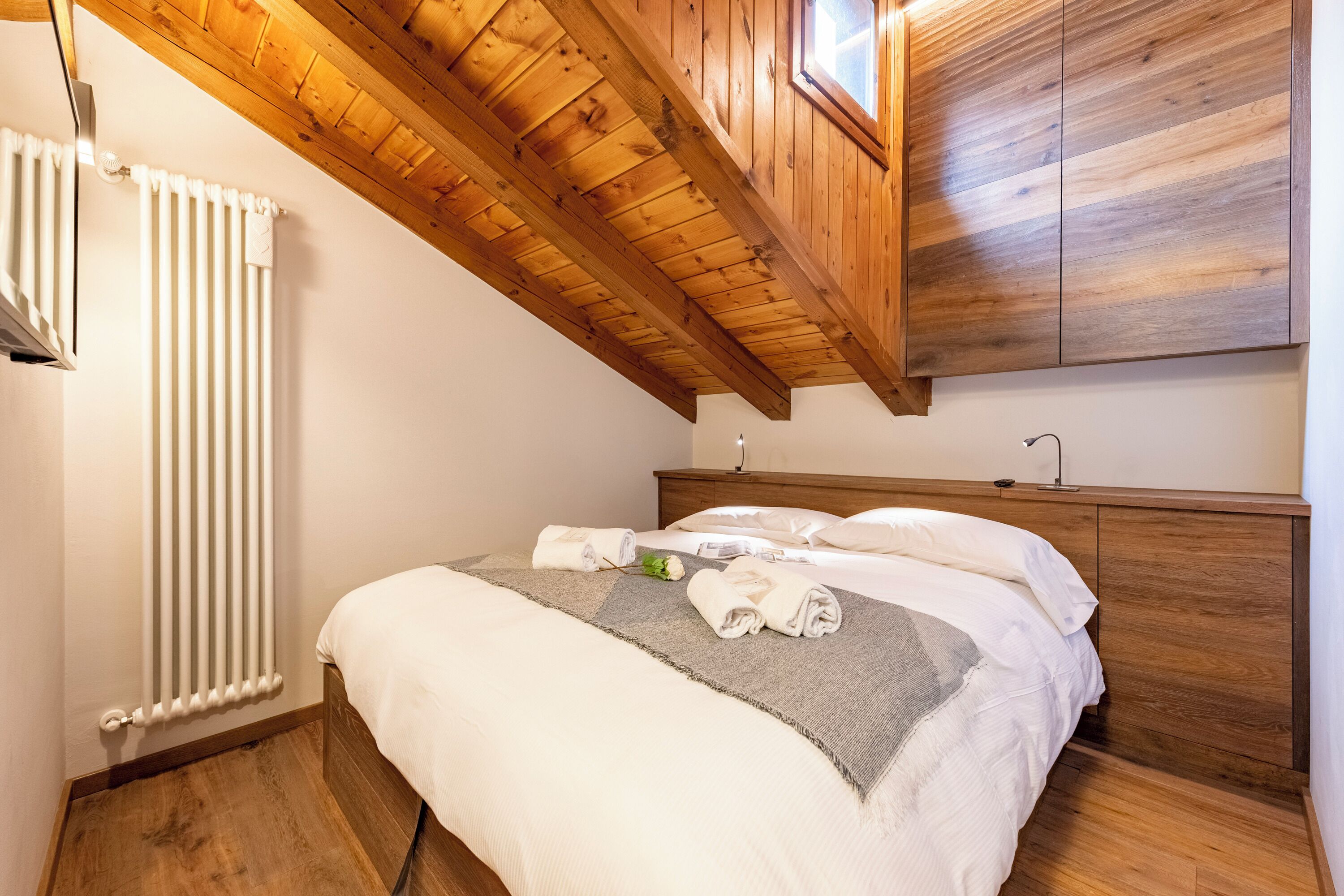 A neatly made bed with white linens and a gray throw, wooden headboard, and a wooden ceiling with a skylight.