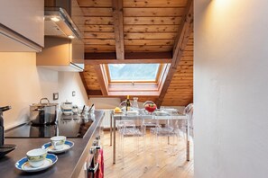 Una cucina moderna con un lucernario, travi in legno a soffitto e zona pranzo con sedie trasparenti.