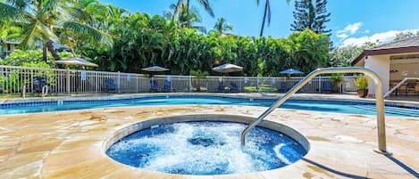 A swimming pool with a hot tub, surrounded by palm trees and lounge chairs.