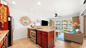 Eine moderne Küche mit Kochinsel, Holzschränken und einem eingebauten Backofen. Ein Essbereich mit Tisch und Stühlen sowie ein Wohnzimmer mit Sofa und Blick auf Balkone.