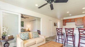 A living room with a sofa, a coffee table, and a dining area with chairs. - Privacy, Ocean View! Modern Kitchen, WiFi, Flat Screen, Lanai–Kauai Kailani K212 (Kapa'a)